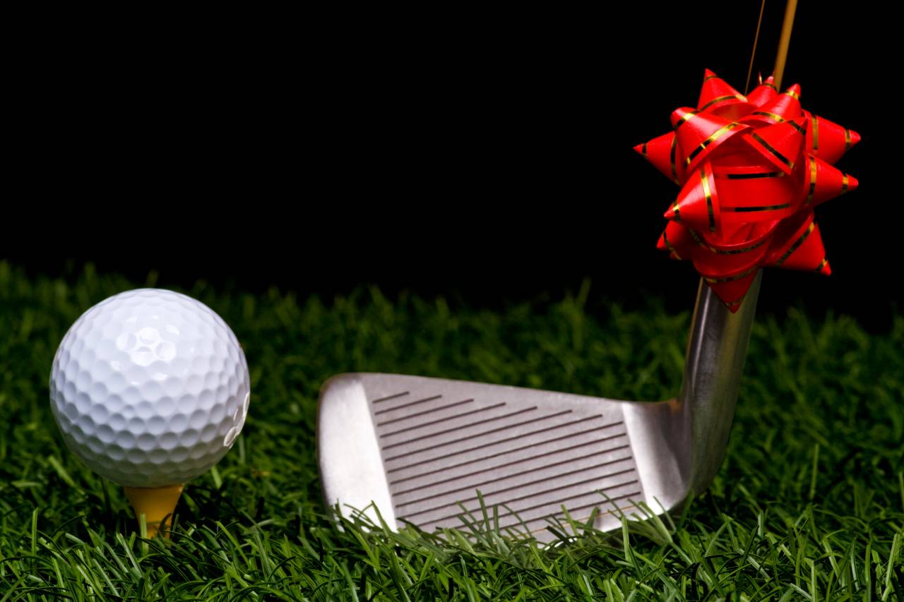 golf ball tee'd up on a wooden tee with a iron with a bow on it.